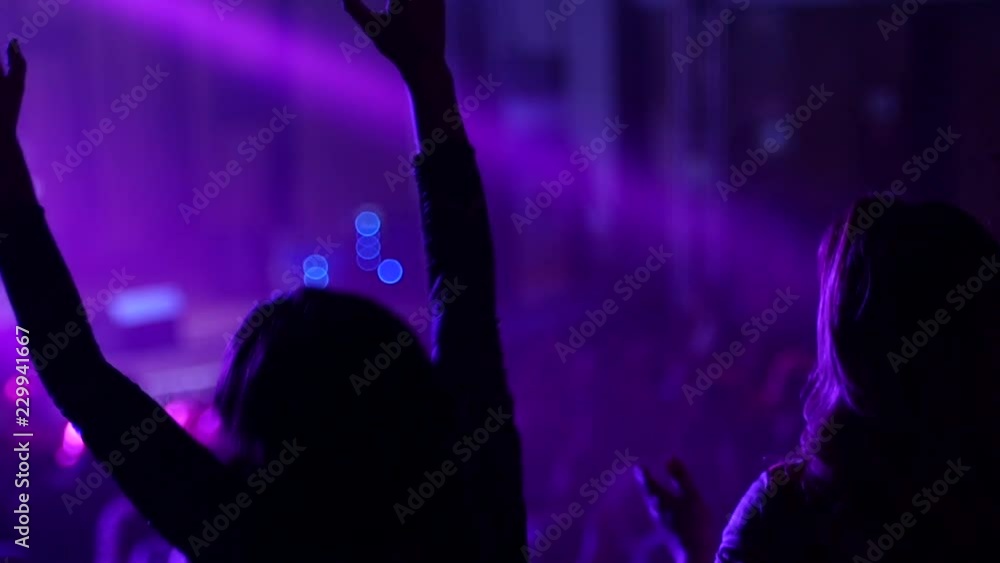 Dancing girl fan silhouettes on a concert flashing light cheerful hands in air