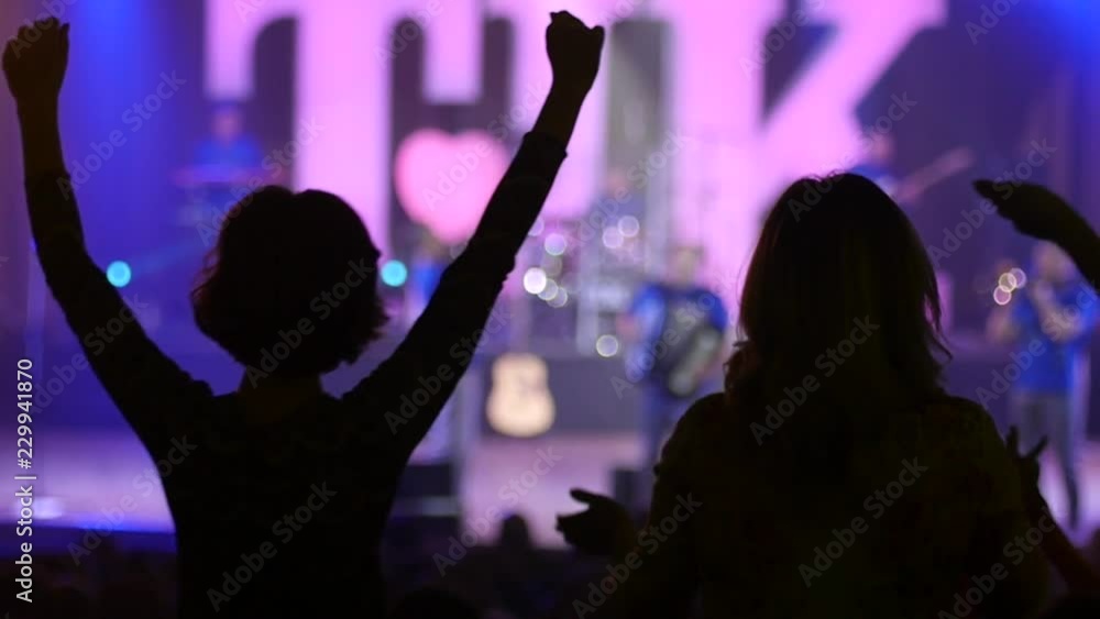 Dancing girl fan silhouettes on a concert flashing light cheerful hands in air