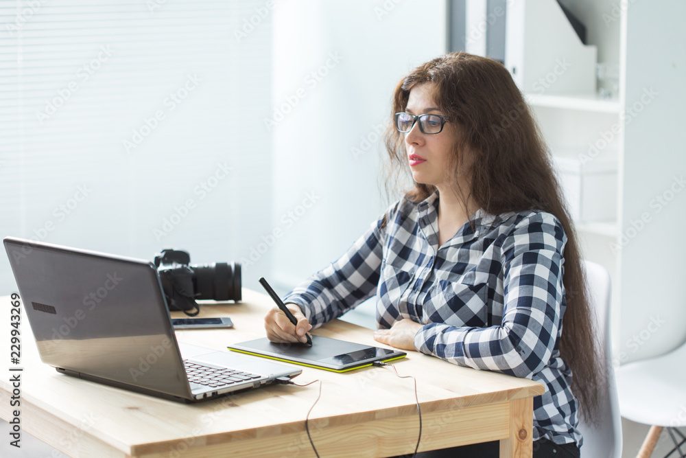Working, business, technology and designer concept - young woman using tablet and watching in laptop Working, business, technology and designer concept - young woman using tablet and watching in laptop