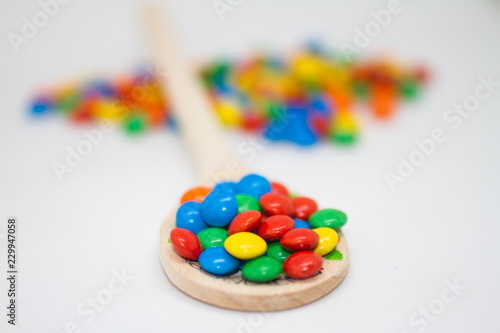 colorful chocolate buttons in a wooden spoon on a white background