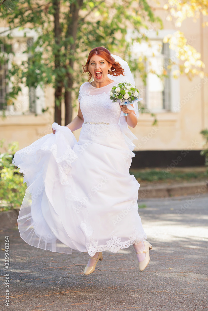 Beautiful redhead bride with bouquet outdoor. Happy bride jumping and having fun outdoors. Beautiful bride posing in her wedding
