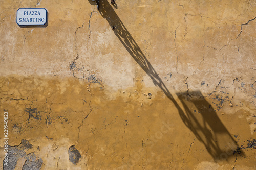 Street lamp casting a shadow on an old weathered wall in Piazza San Martino in Lucca, Tuscany, Italy © Michael Evans