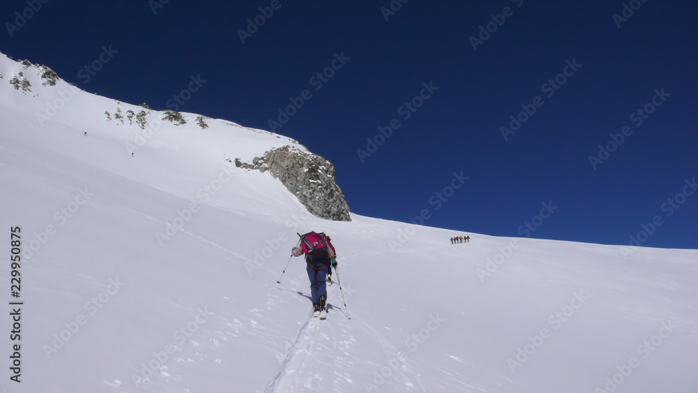 several backcountry skiers hike and climb to a remote moutain peak in Switzerland on a beautiful winter day