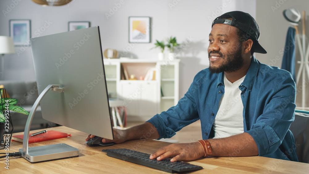 Portrait of the Stylish African American Working on a Personal Computer while Sitting at His Desk at Home. Portrait of the Stylish African American Working on a Personal Computer while Sitting at His Desk at Home.