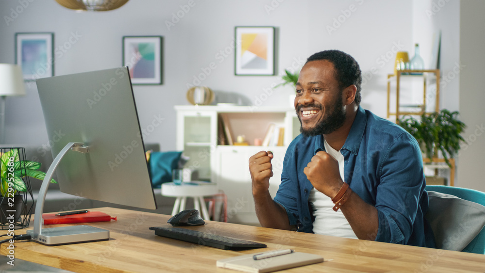 Obraz premium Excited Young Man Uses Personal Computer at Home, Wins Big, Does 