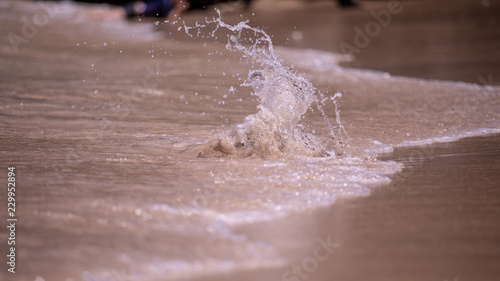 Water splashing over a small stone on a sand beach