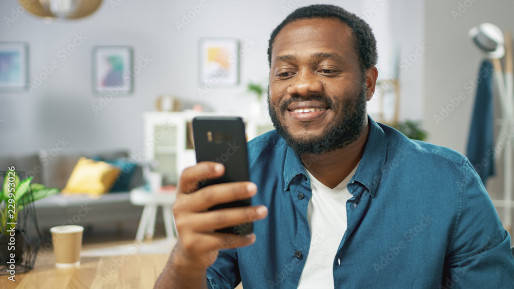 Portrait of the Handsome Young Man Using Smartphone, Browsing in Internet, Checking Social Networks, Scrolling Newsfeed while Sitting At Home. Portrait of the Handsome Young Man Using Smartphone, Browsing in Internet, Checking Social Networks, Scrolling Newsfeed while Sitting At Home.