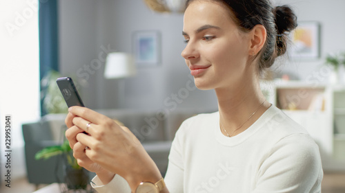 Portrait of the Beautiful Young Woman Using Smartphone, Browsing in Internet, Checking Social Networks while Sitting At Home.