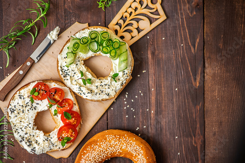 Bagels with cream cheese, sesame, tomato and cucumber on a wooden Board. Top view flat lay. With copy space