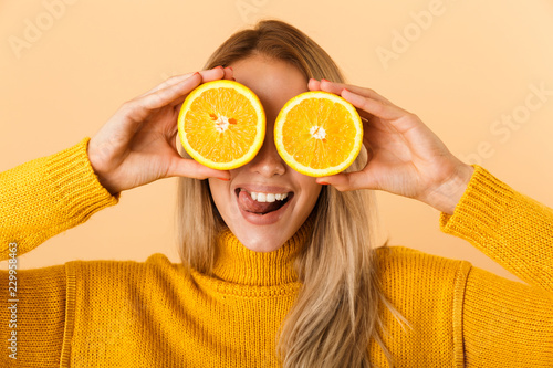 Beautiful woman covering eyes with citrus lemons posing isolated over yellow wall background.