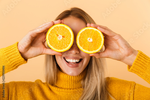 Beautiful woman covering eyes with citrus lemons posing isolated over yellow wall background.