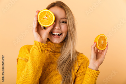 Foto Beautiful woman covering eyes with citrus lemons posing isolated over yellow wall background