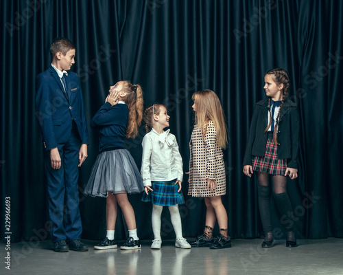 Cute surprised stylish children on dark background. Beautiful stylish teen girls and boy standing together and posing on the school stage in front of the curtain. Classic style. Kids fashion and