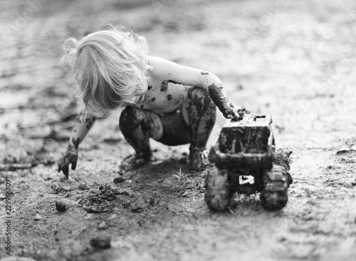 young child completely covered in mud playing with truck photo