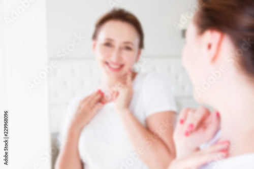 Blurred background of Middle age woman looking in mirror on face. Wrinkles and anti aging skin care concept. Selective focus