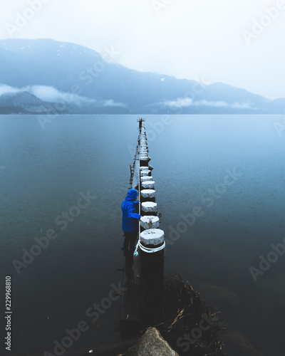 A young person walks along a wooden structure above the water on a rainy and foggy day in Squamish BC