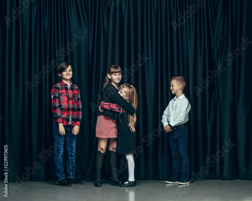 Cute surprised stylish children on dark background. Beautiful stylish teen girls and boy standing together and posing on the school stage in front of the curtain. Classic style. Kids fashion and