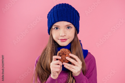 Cute girl in knitted hat eating Christmas biscuits.child model diet pink background in studio