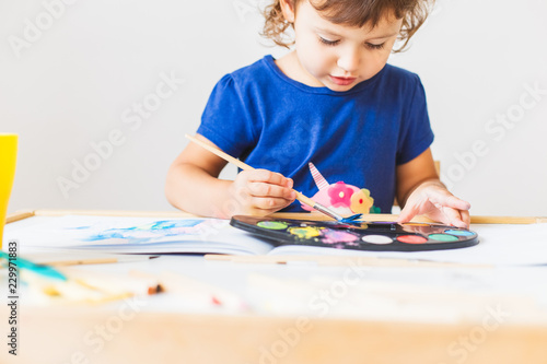 3 years girl painting at the small table at home.