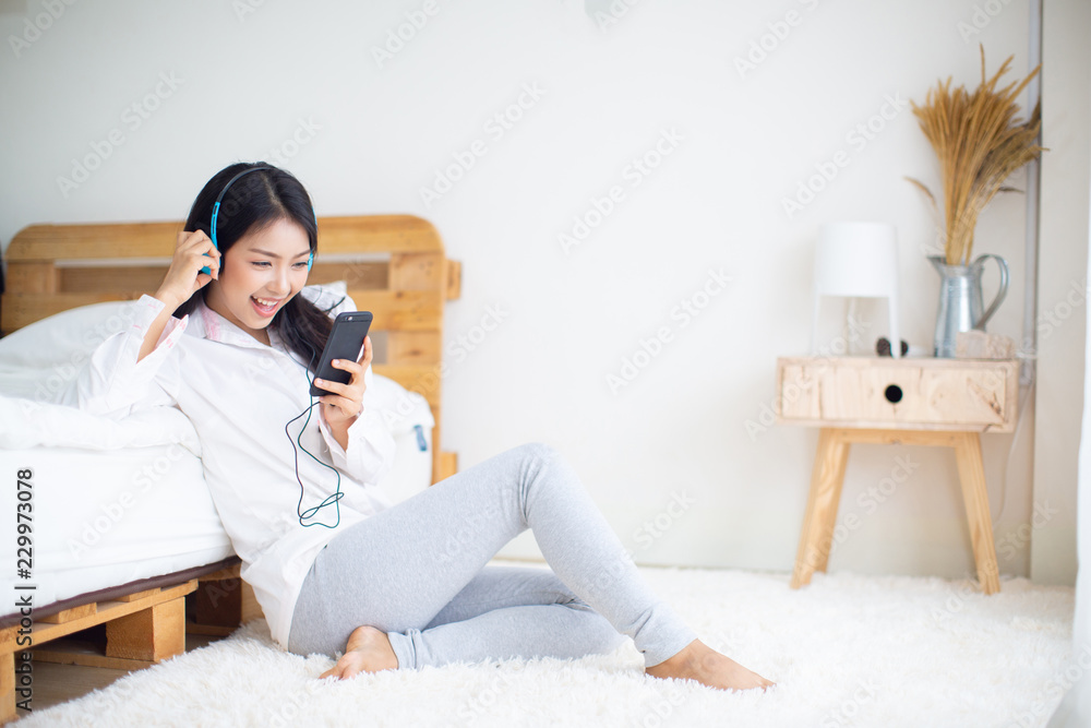 Fototapeta premium Happy woman in headphones listening to music from smart phone,relaxation in bedroom