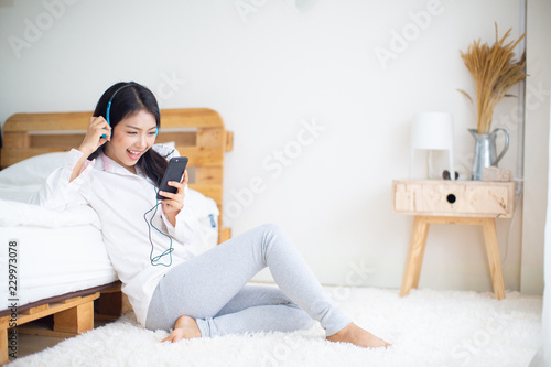 Happy woman in headphones listening to music from smart phone,relaxation in bedroom