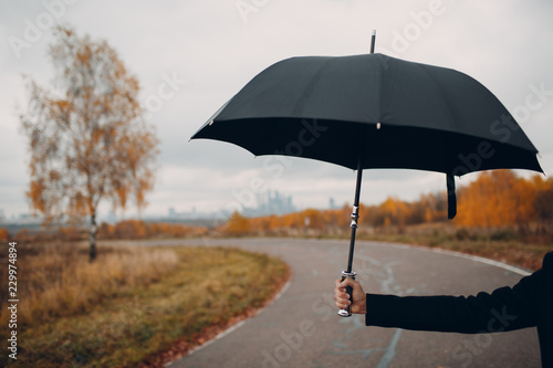 Young man in black holds umbrella in hand close up