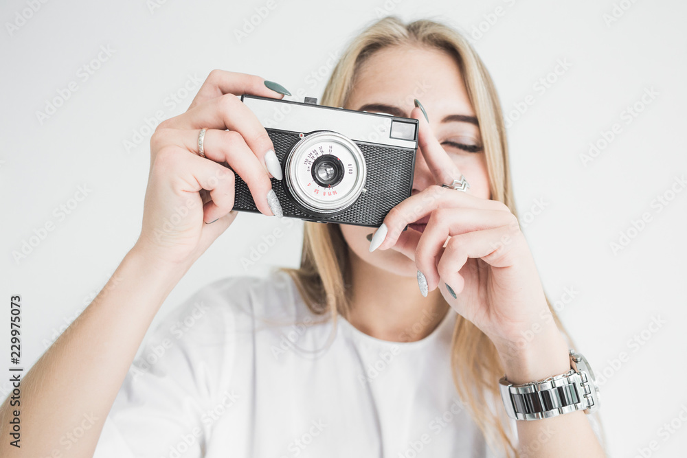 Portrait of a young stylish blonde girl using and taking pictures on an old vintage camera on a white background Portrait of a young stylish blonde girl using and taking pictures on an old vintage camera on a white background