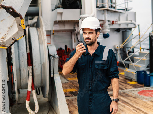 Marine Deck Officer or Chief mate on deck of vessel or ship . He holds VHF walkie-talkie radio in hands. Ship communication photo