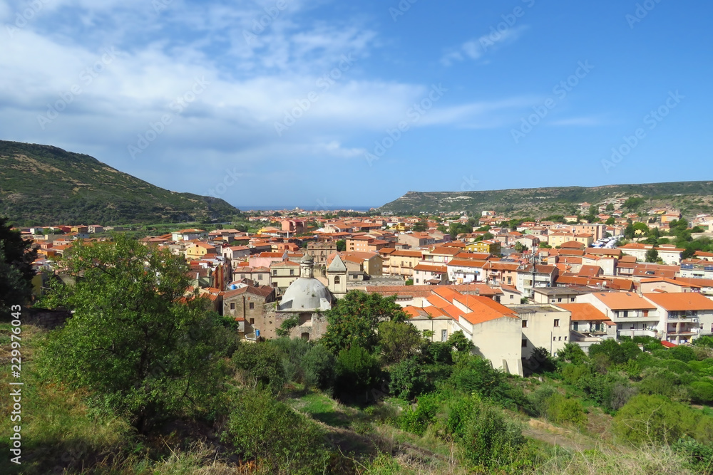 View over the old town of Bosa, the church and typical houses with red roofs surrounded by mountains and the Mediterranean Sea in the distance, Sardinia, Italy