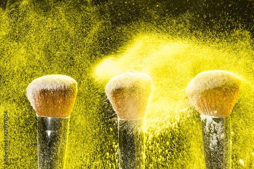 Mineral make up and objects concept - Three make up brushers in yellow dust over dark background
