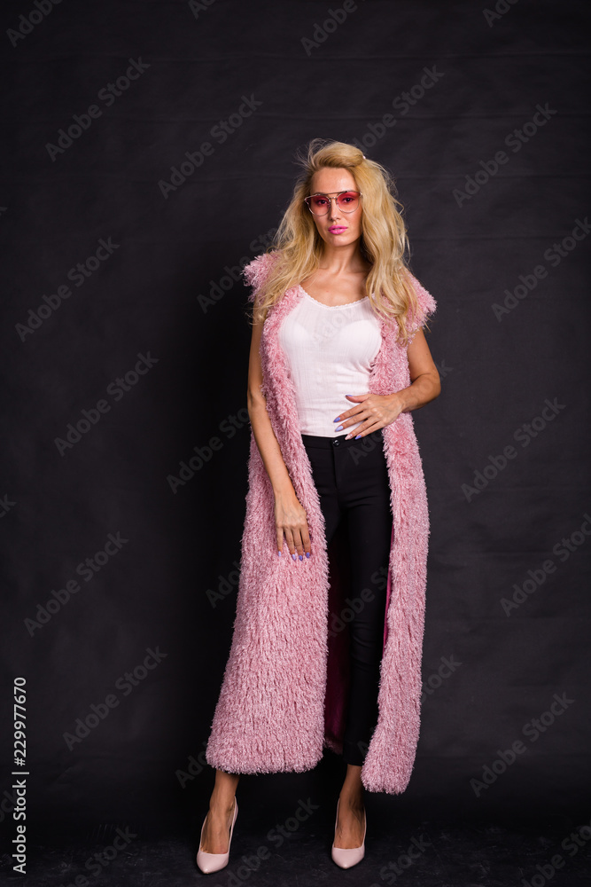 Fashion and people concept - young blonde woman in glasses standing in pink fur coat and smiling Fashion and people concept - young blonde woman in glasses standing in pink fur coat and smiling
