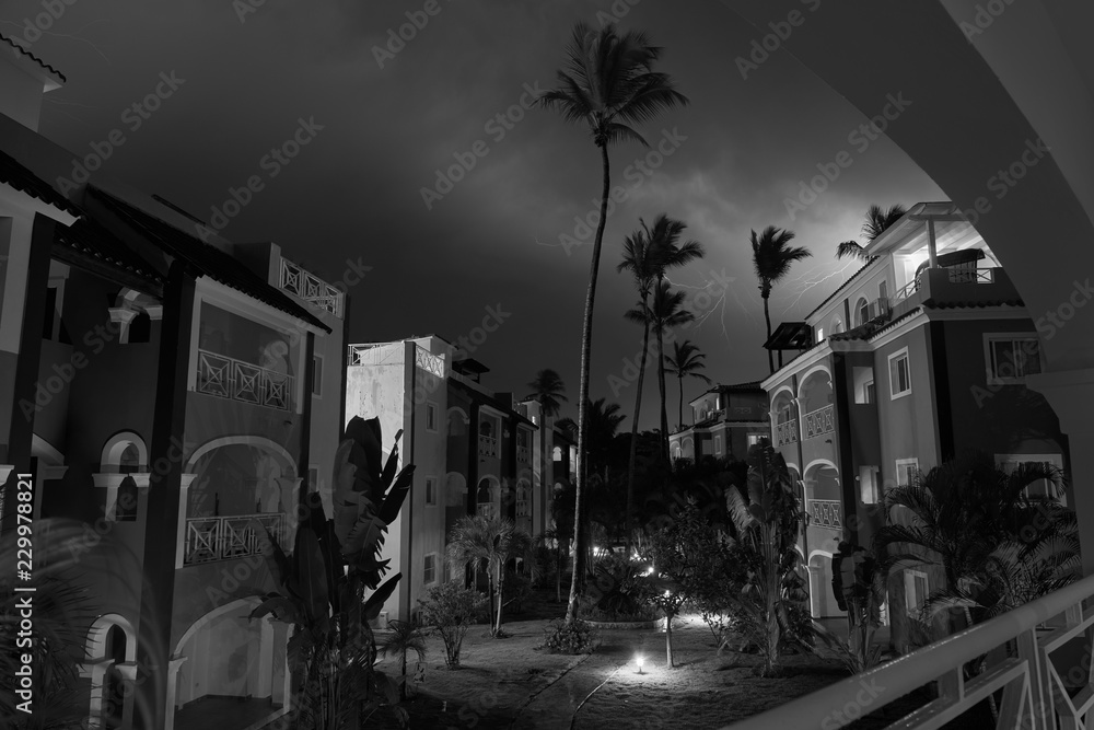 Monocrome long exposure shot of residence in small town Bavaro. Shot made in stormy night with heavy cloudy sky and lightnings in it. Path through te residence is lighten with small lanterns. - obrazy, fototapety, plakaty 