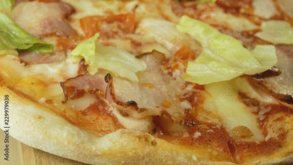 pizza with bacon, cheese, tomatoes, red onions and leaves, rotating on wooden background, close-up pizza with bacon, cheese, tomatoes, red onions and leaves, rotating on wooden background, close-up