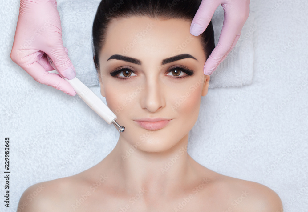 The cosmetologist makes the apparatus a procedure of Microcurrent therapy of a beautiful, young woman in a beauty salon. Cosmetology and professional skin care.