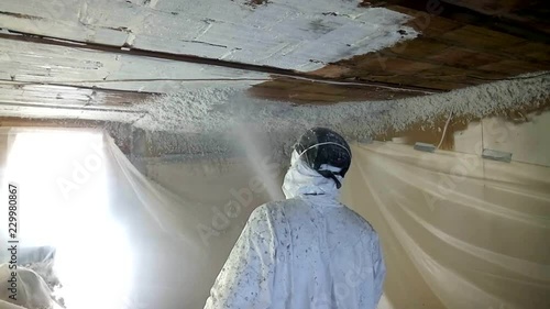 Workman spraying foam insulation material into ceiling in old cave.