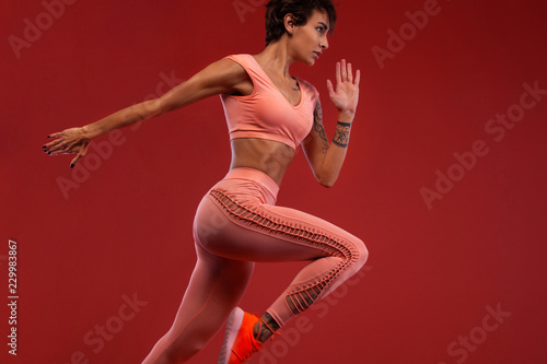 A strong athletic, woman sprinter or runner, running on red background wearing sportswear. Fitness and sport motivation. photo