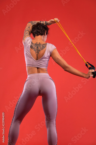 Fitness and sport motivation.. Strong and fit athletic, woman with bands or expander posing on red background in sportswear.