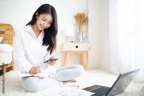 Happy casual beautiful woman working on a laptop and smart phone sitting in the bedroom