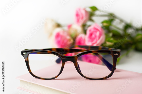 Glasses on the table on the pink book on the background of flowers.
