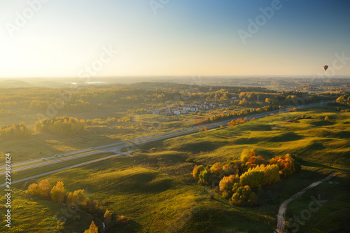 Colorful hot air balloon flying over fields surrounding Vilnius city on sunny autumn evening.