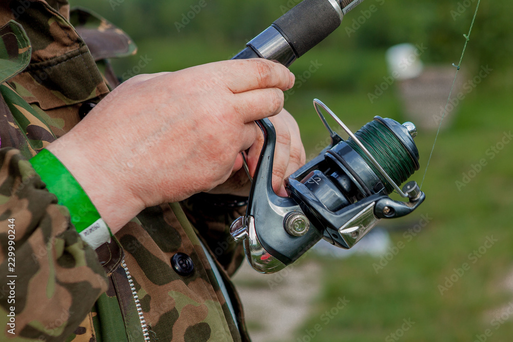 A fisherman with a fishing rod. Close-up of a hand holding a spinning rod and twisting a coil. Colorful view, blurred background, selective focus