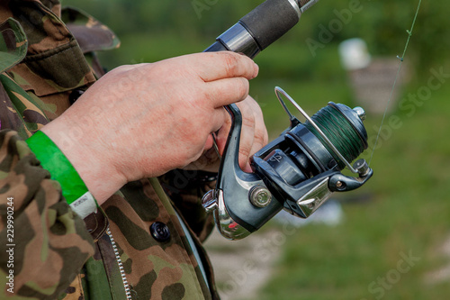 A fisherman with a fishing rod. Close-up of a hand holding a spinning rod and twisting a coil. Colorful view, blurred background, selective focus