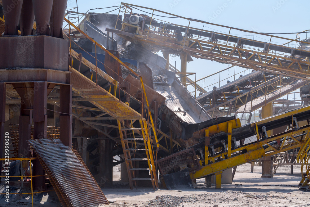 Naklejka premium Crushing machinery, cone type rock crusher, conveying crushed granite gravel stone in a quarry open pit mining. Processing plant for crushed stone and gravel. Mining and Quarry mining equipment.