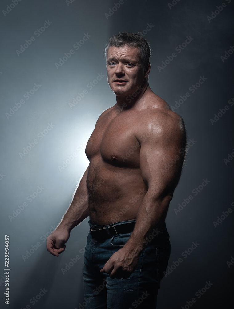 Fototapeta premium Powerful muscular bodybuilder posing on a black background. concept of strength and health