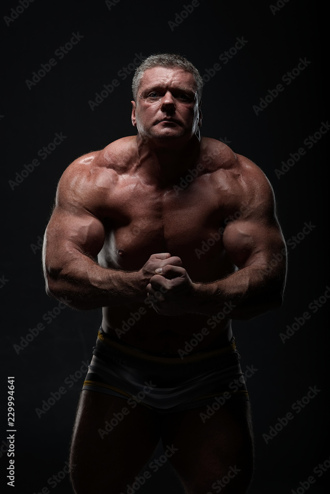 powerful muscular man shows biceps on a black background. Strength and fitness concept