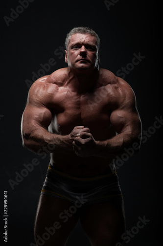 powerful muscular man shows biceps on a black background. Strength and fitness concept © Vladimir