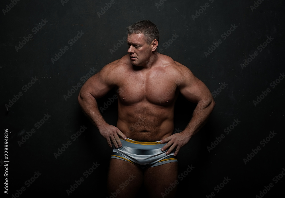 Fototapeta premium muscular man shows off his body near black grunge wall