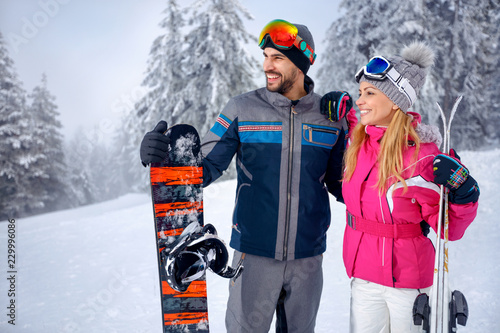 smiling couple skiing and snowboarding enjoying in snowy mountains together