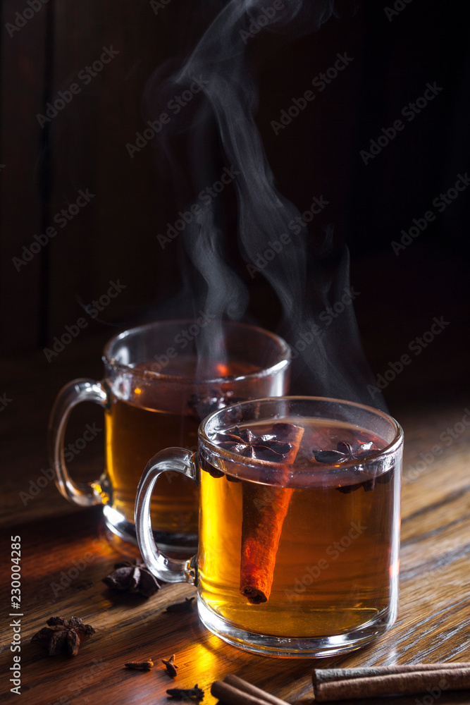 2 glass mugs of steaming hot spiced cider on dark wood 2 glass mugs of steaming hot spiced cider on dark wood
