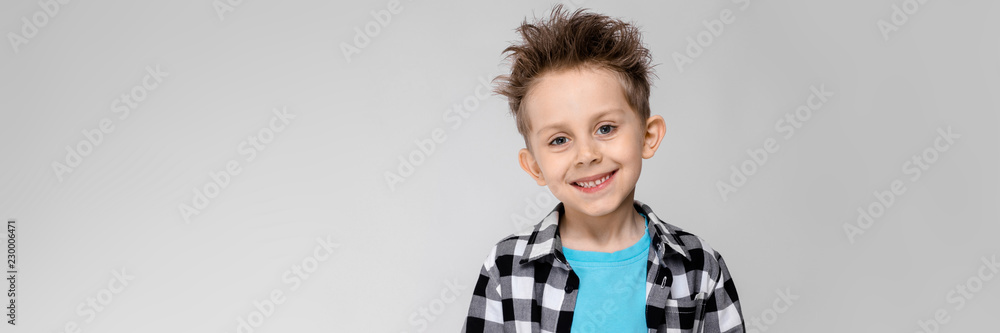 A handsome boy in a plaid shirt, blue shirt and jeans stands on a gray background. The boy is holding a phone A handsome boy in a plaid shirt, blue shirt and jeans stands on a gray background. The boy is holding a phone